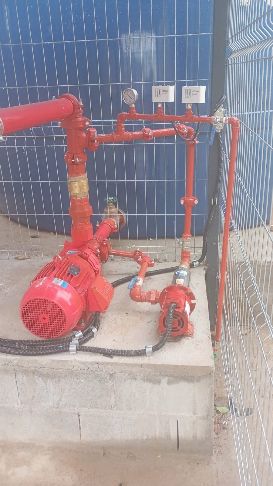 Conjunto de bomba de incêndio e rede hidráulica vermelha instalada em base de concreto
